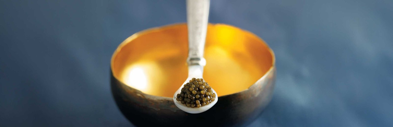 Caviar on a mother-of-pearl spoon above a gilded bowl