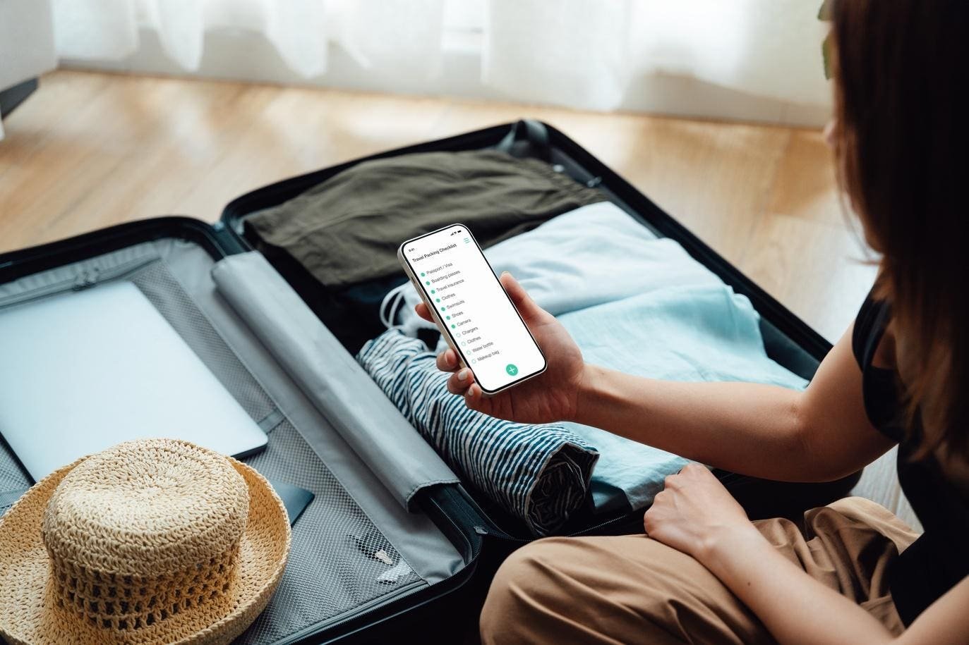 A traveller packing a suitcase while checking a smartphone