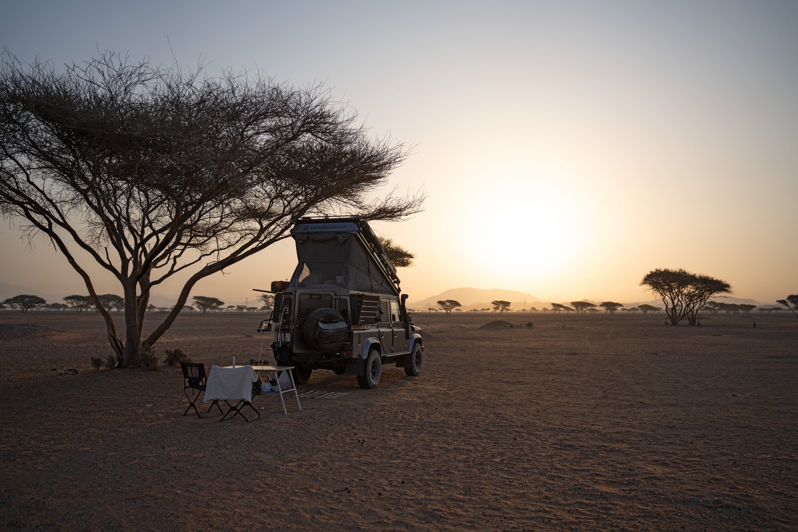 Land Rover Defender 110 at a camp at sunset, dust in the air